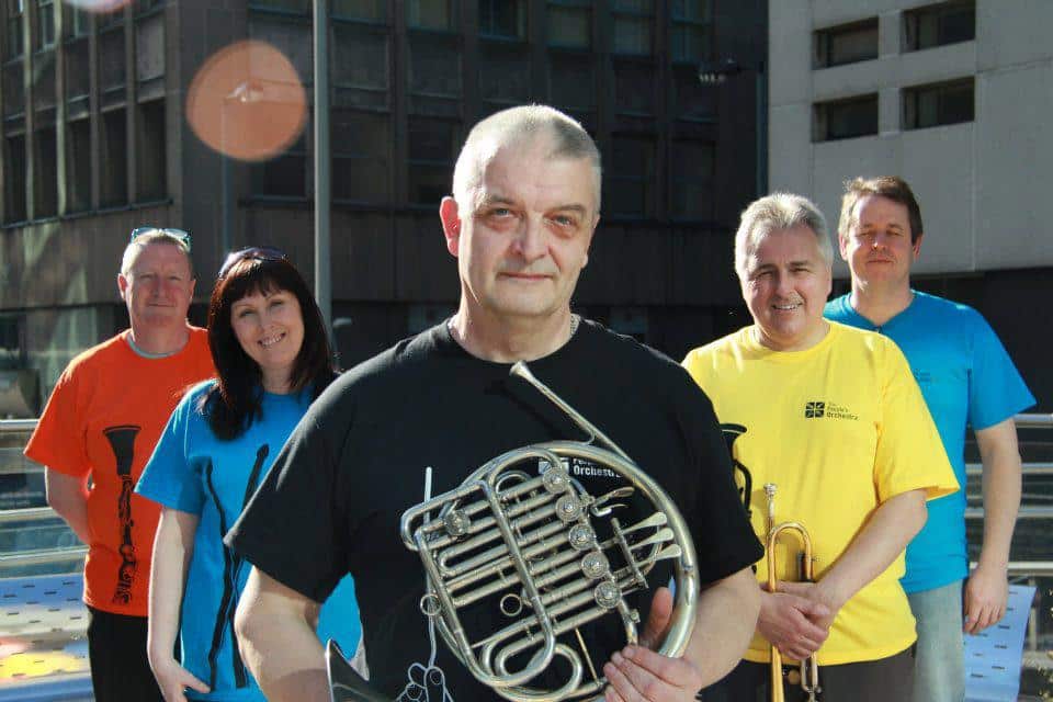 The first TPO musicians stand with their instruments outside in Birmingham City Centre in March 2012. Andy Sandham stands front in centre with his french horn.