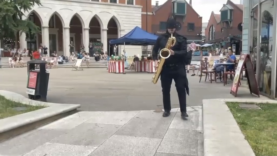 Batman cosplay playing the saxophone.