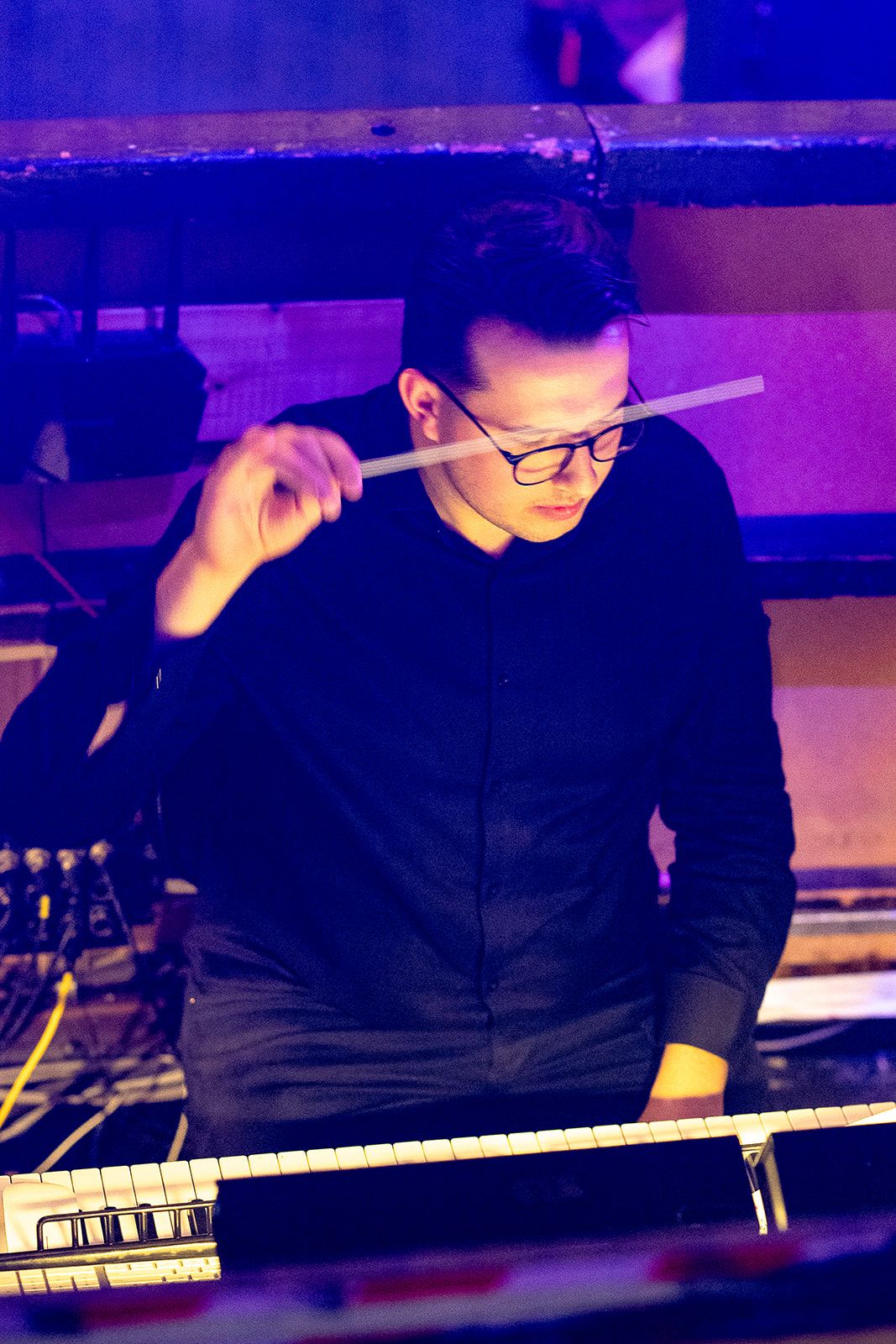 Joe Allen, conductor of TPSC York, conducting with a baton. He is wearing a black suit and black glasses.