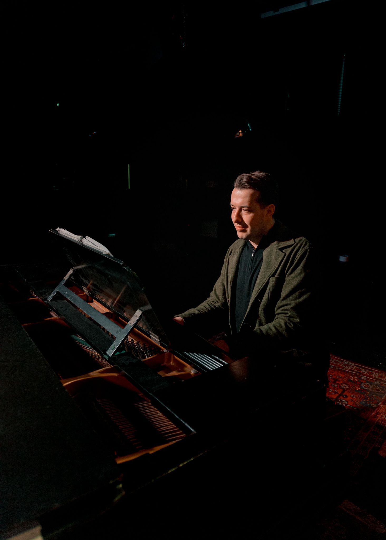 Joe Allen, a white British conductor of The People's Show Choir York, is conducting an ensemble. He is wearing a dark-coloured suit and has brown hair. 