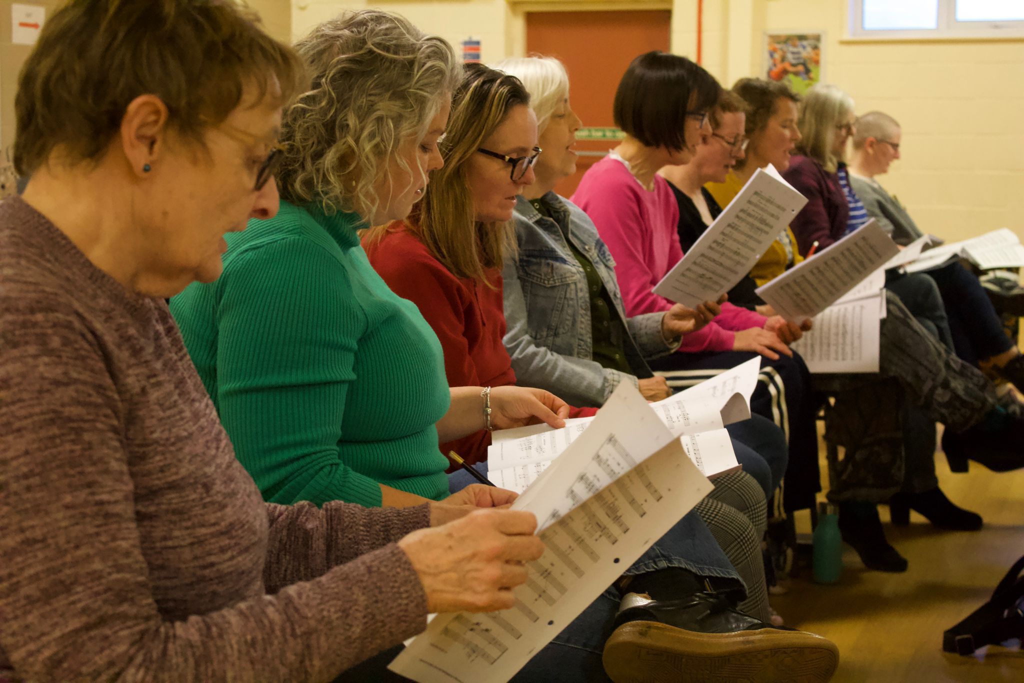 Singers in The People's Show Choir York sat in a rehearsal, reading music sheets on their laps, singing the lyrics.