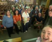 Singers and the Choir Leader of TPSC Leeds are smiling at their first ever rehearsal.