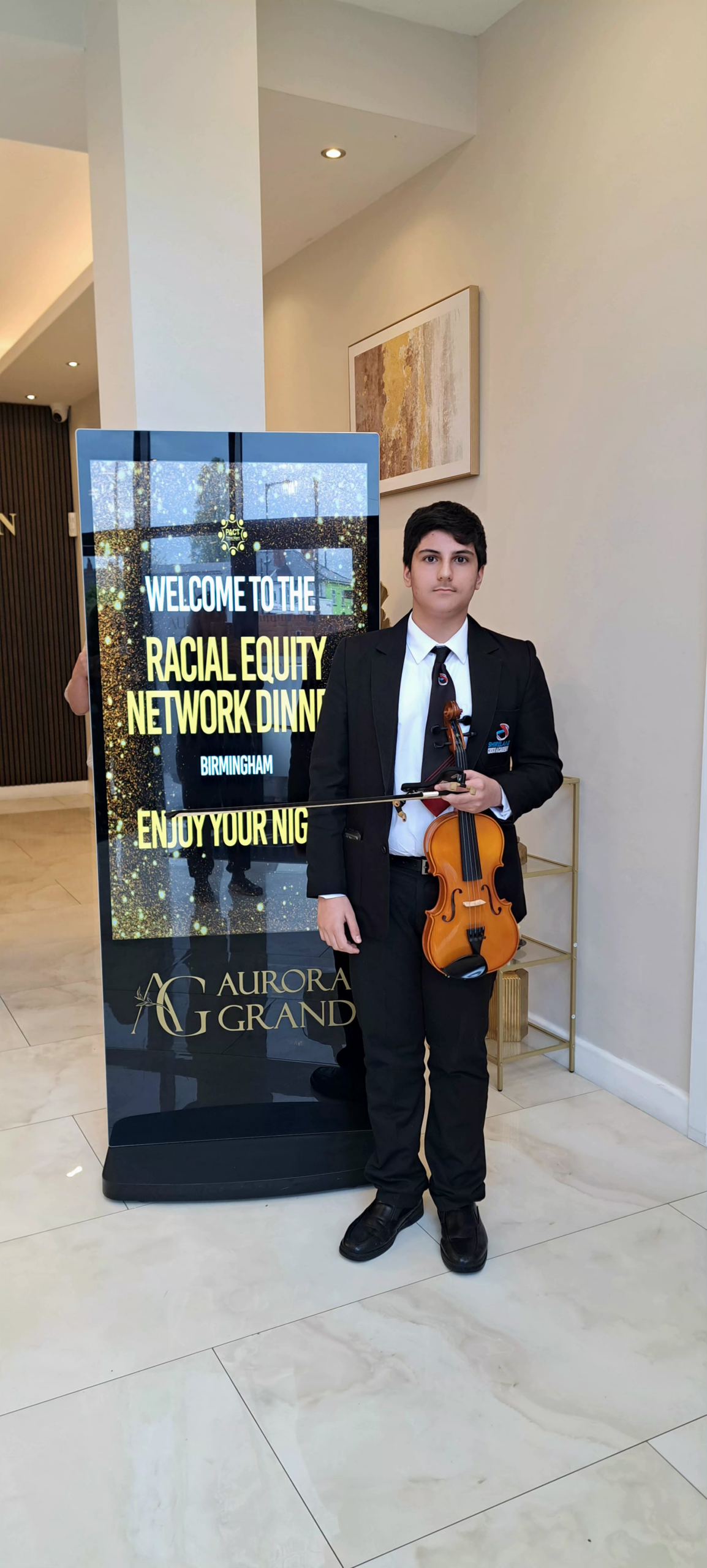 Aman Gill outside a concert hall. He is dressed in a suit holding his violin.