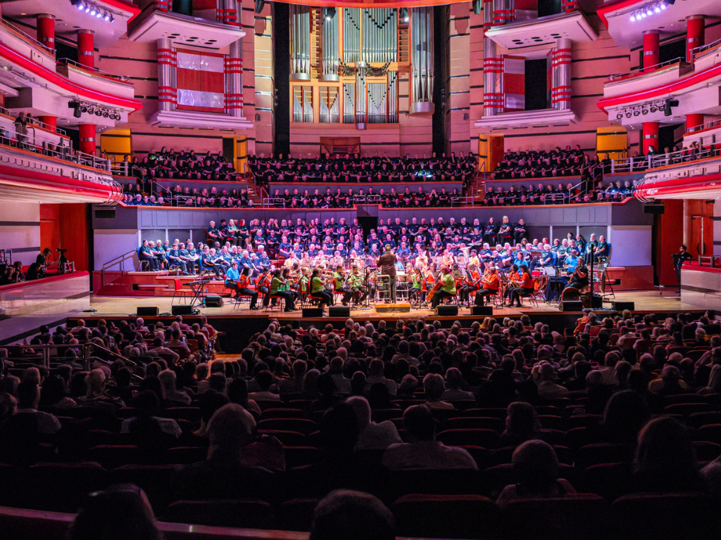 The People's Orchestra and The People's Show Choir performs on the stage and stalls at Birmingham Symphony Hall to the audience.
