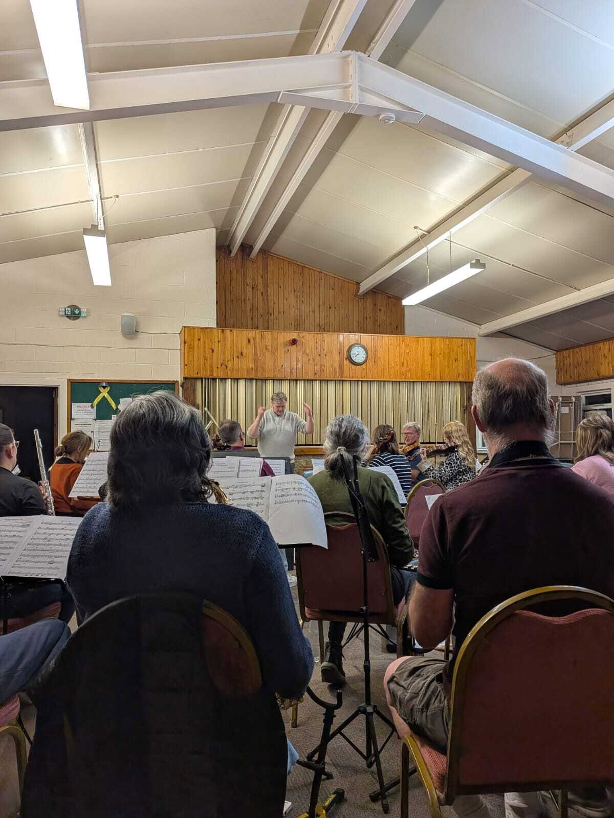 POV of the Conductor Alex McGee conducting Cerddorfa'r Bobl (TPO Carmarthen) orchestra in a village hall.